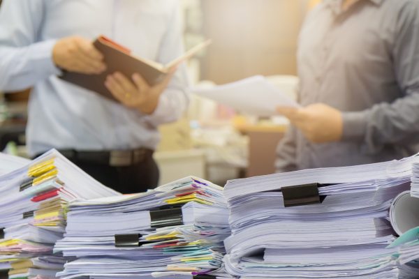 Pile of unfinished documents on office desk with businessman background